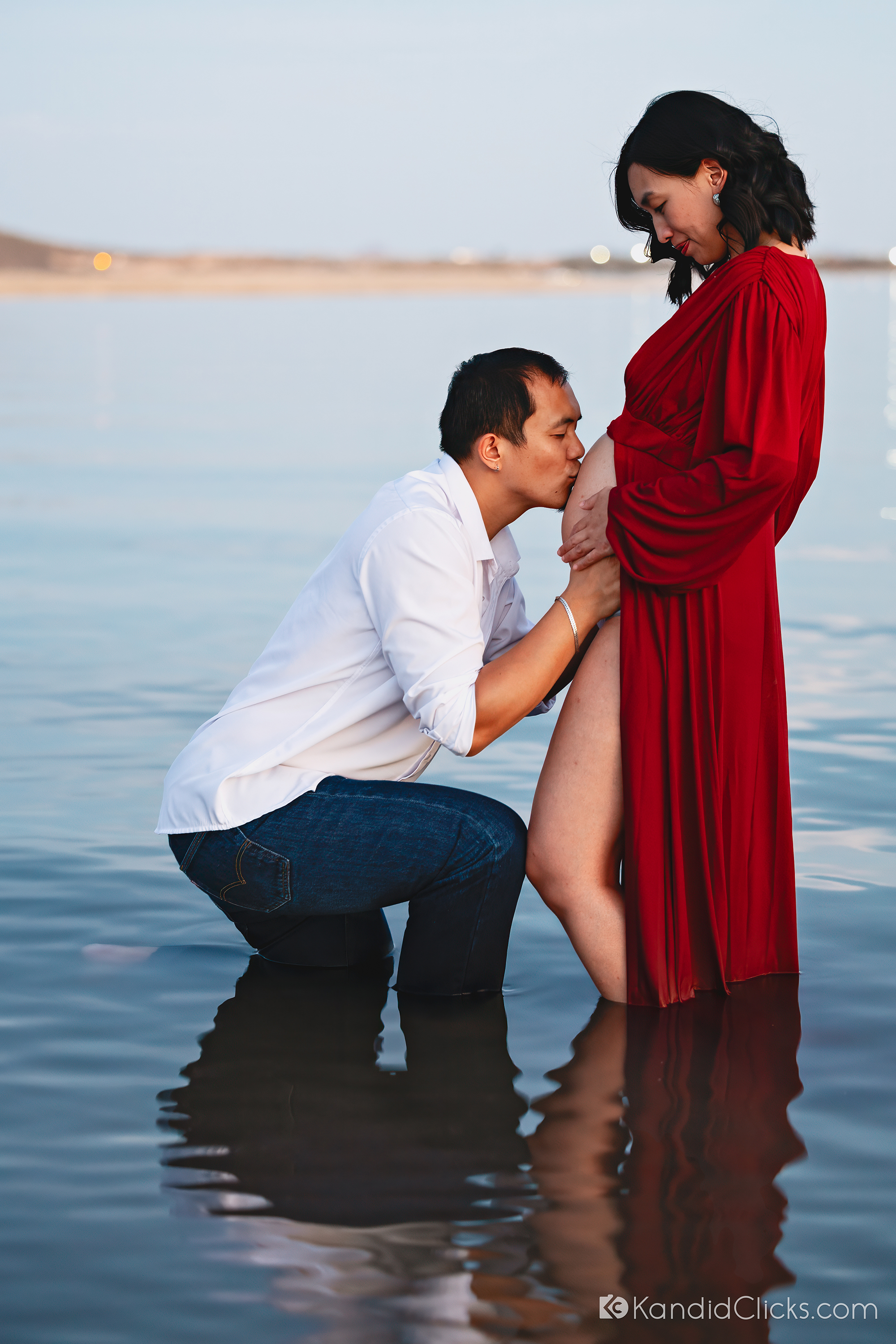 Man kissing pregnant woman's belly during a beach maternity photoshoot at sunset
