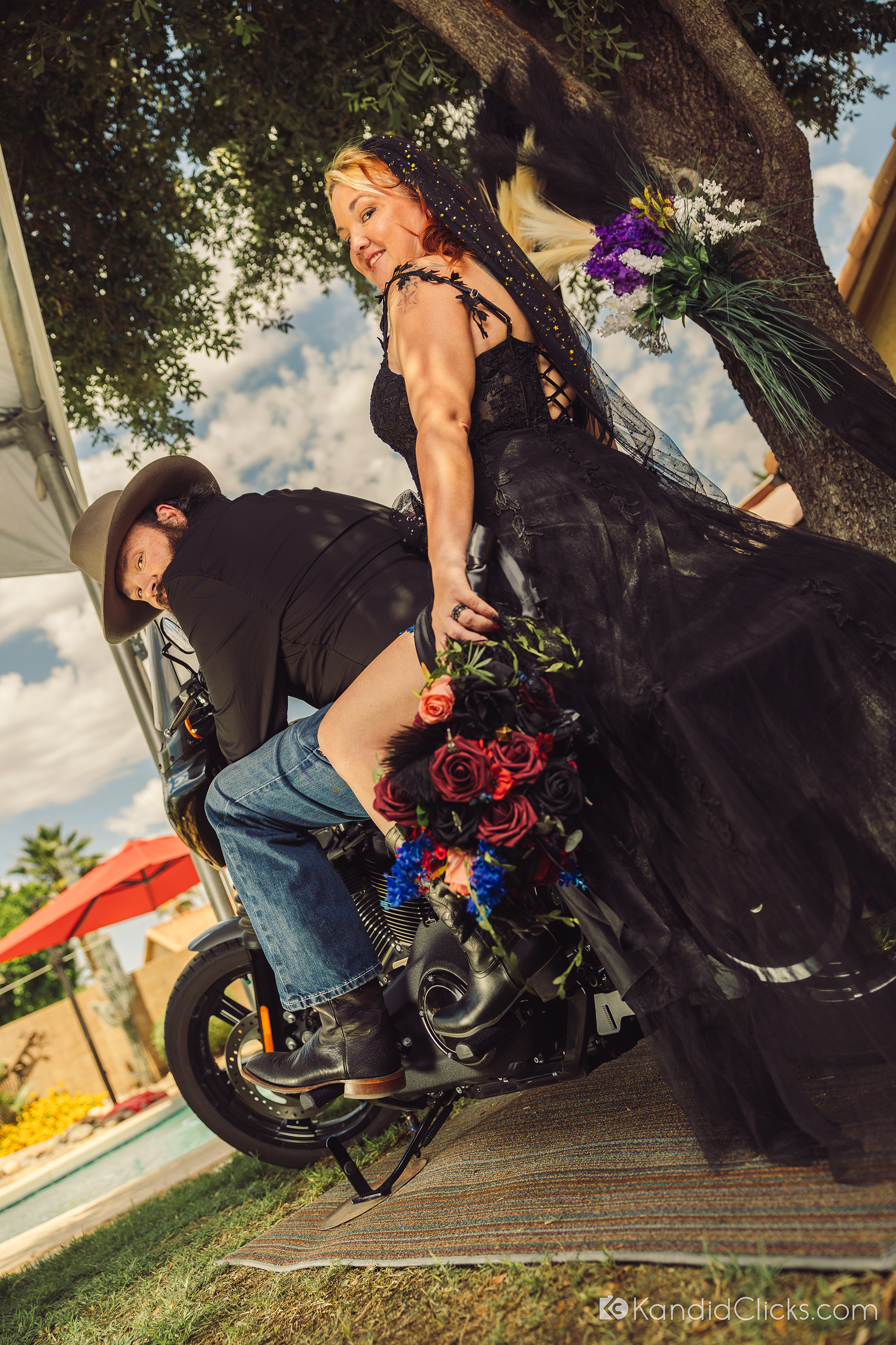 Bride in a black dress riding pillion with groom on a motorcycle at Arizona wedding.