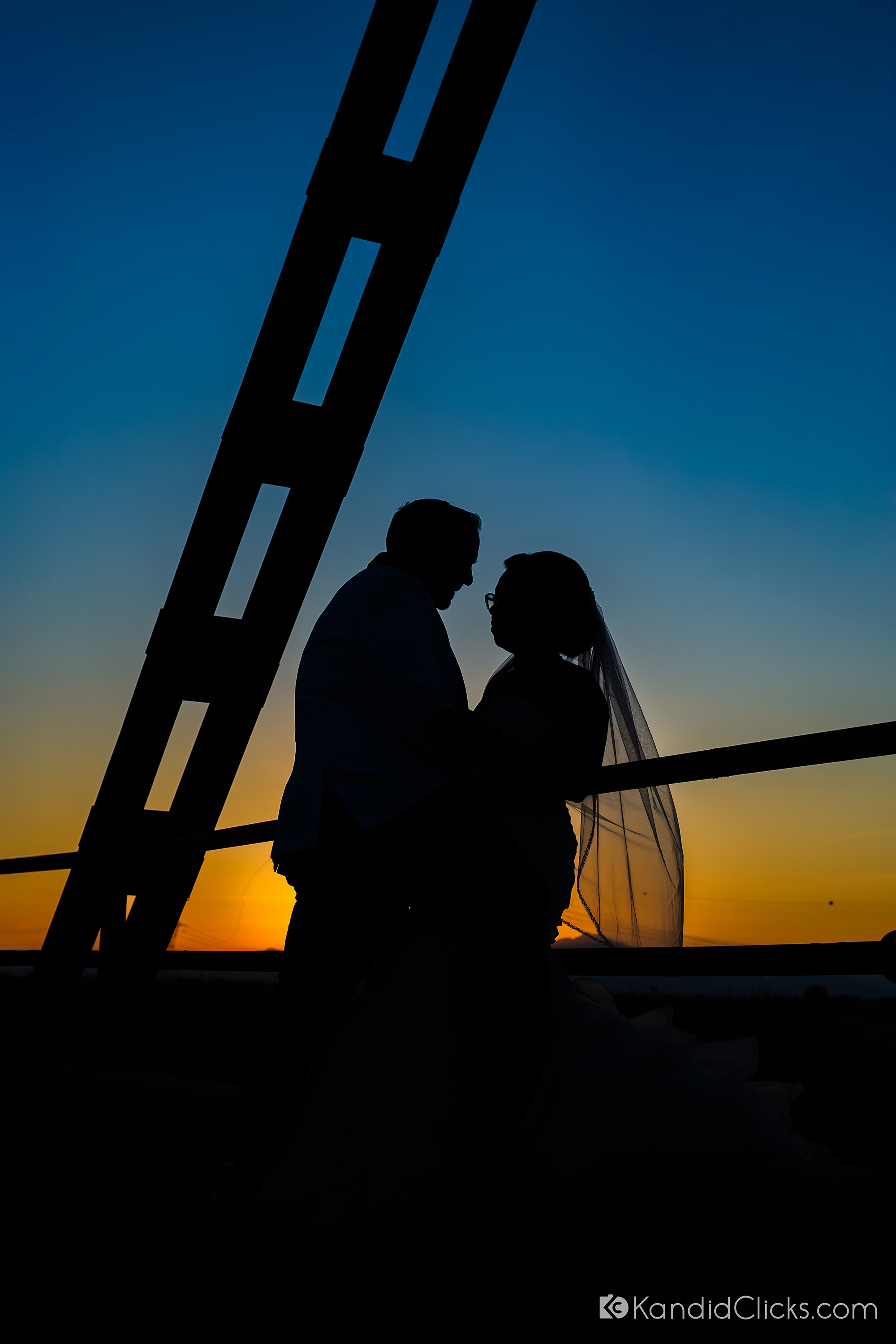Silhouette of bride and groom embracing at sunset on a bridge.