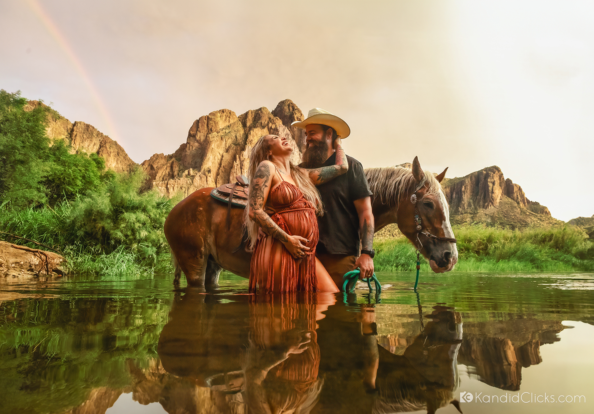 Maternity couple in river with horse, mountain backdrop, and rainbow