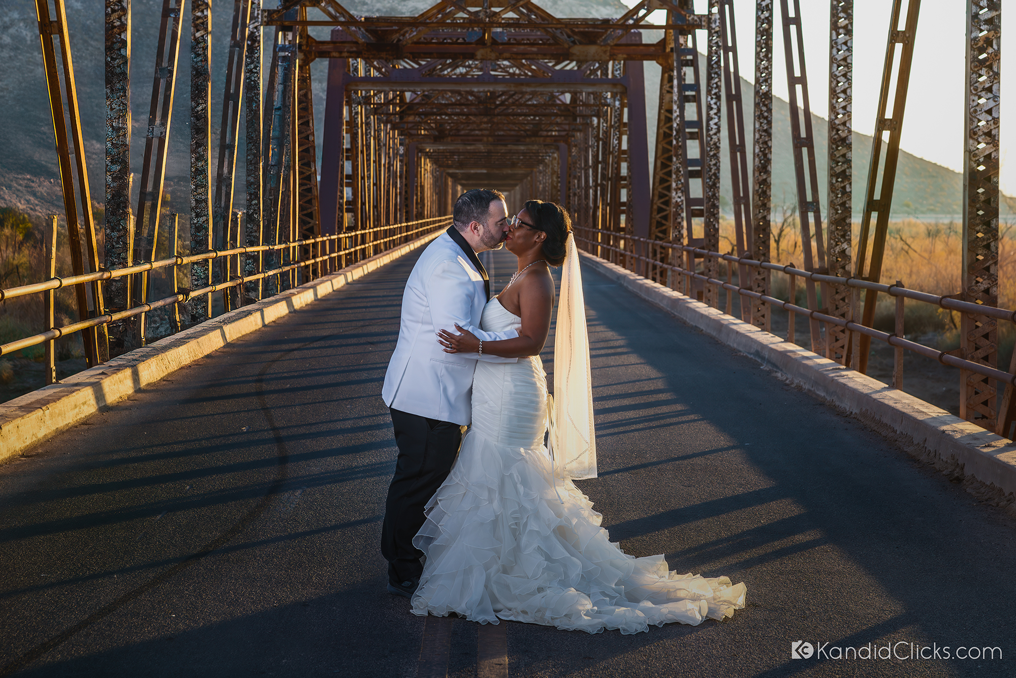 Bride and groom kiss on a rustic bridge during golden hour in Arizona.