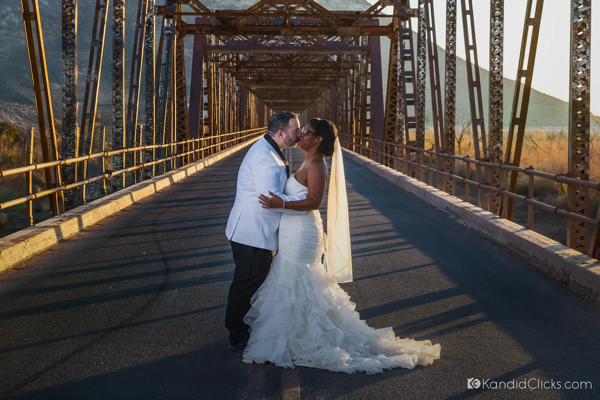 Bride and groom kiss on a rustic bridge during golden hour in Arizona.