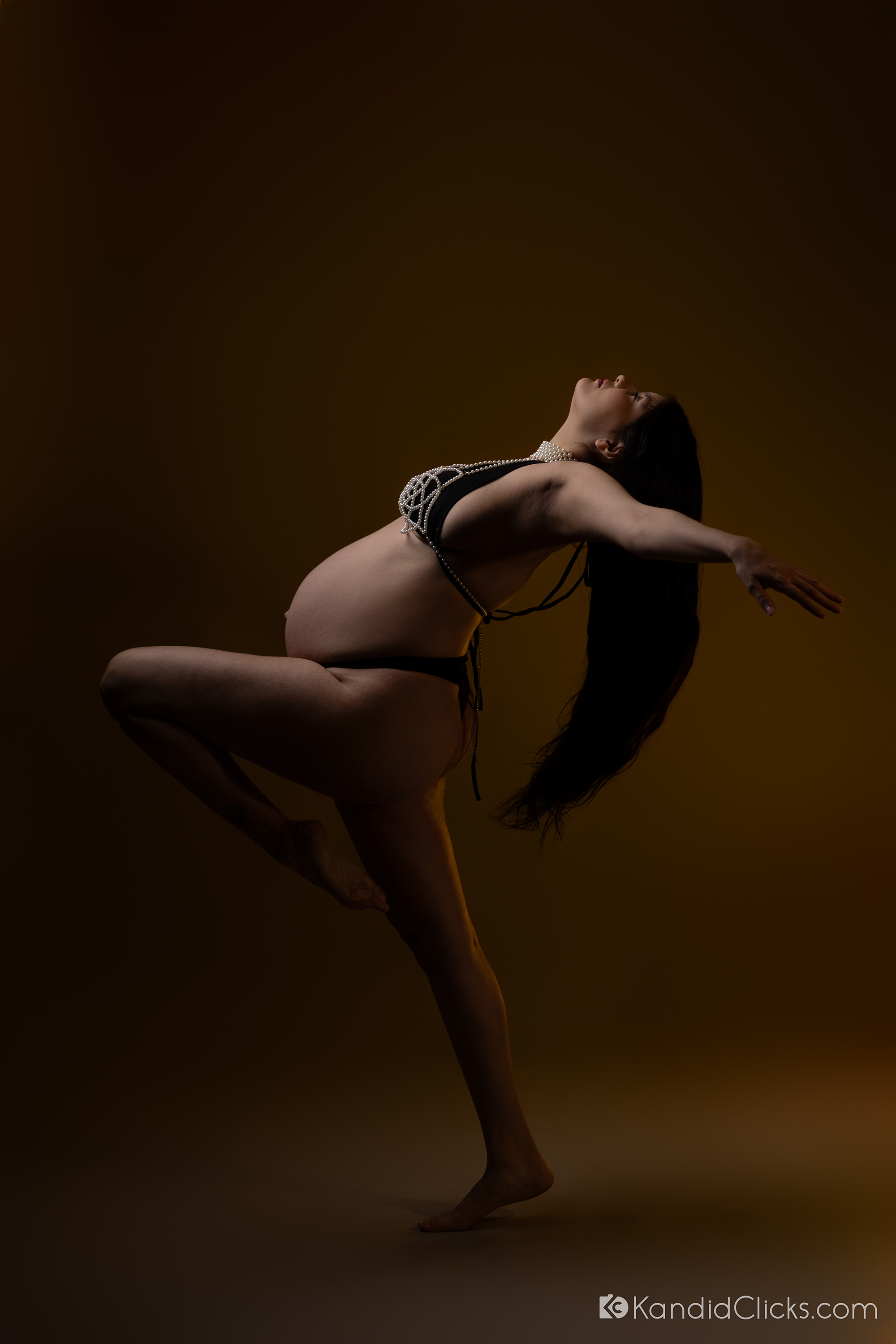 Pregnant woman striking a graceful pose in black lingerie and pearls during a dramatic studio maternity photoshoot
