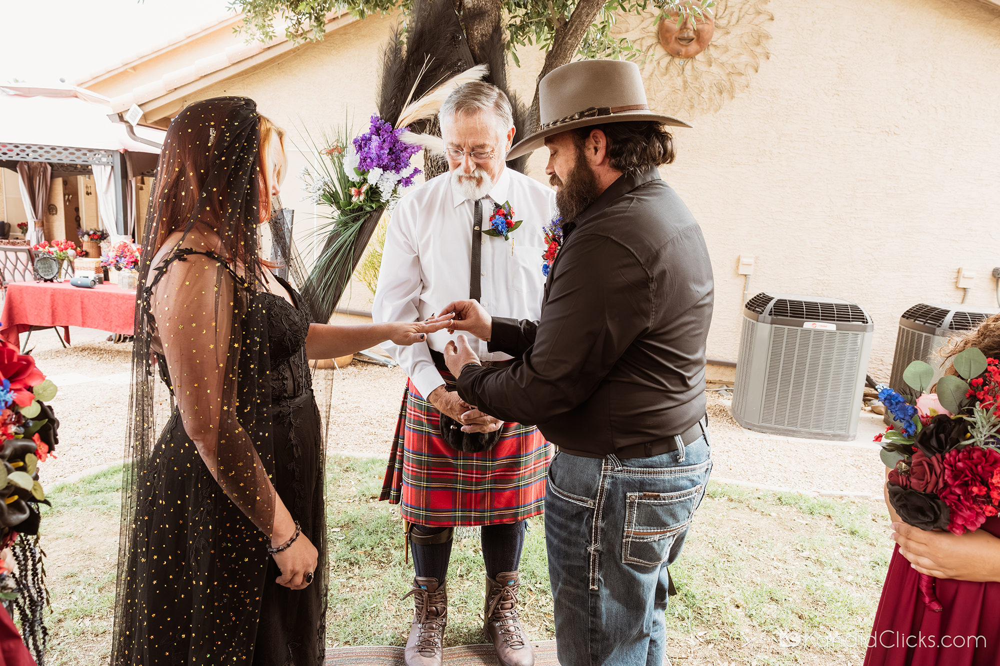 Groom placing ring on bride’s finger during backyard wedding ceremony.