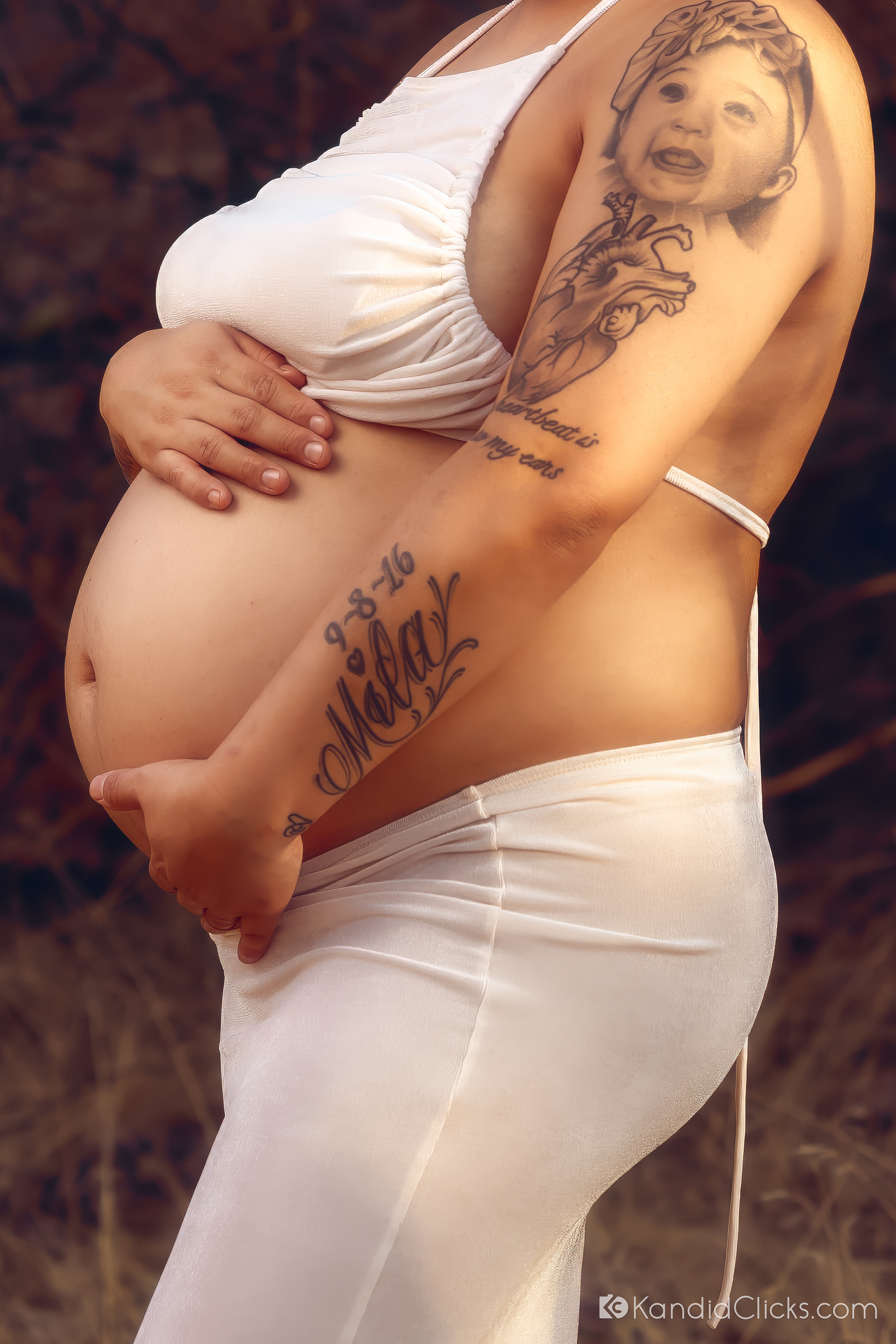 Maternity photographer captures a detailed belly close-up with hands, tattoos, and natural light
