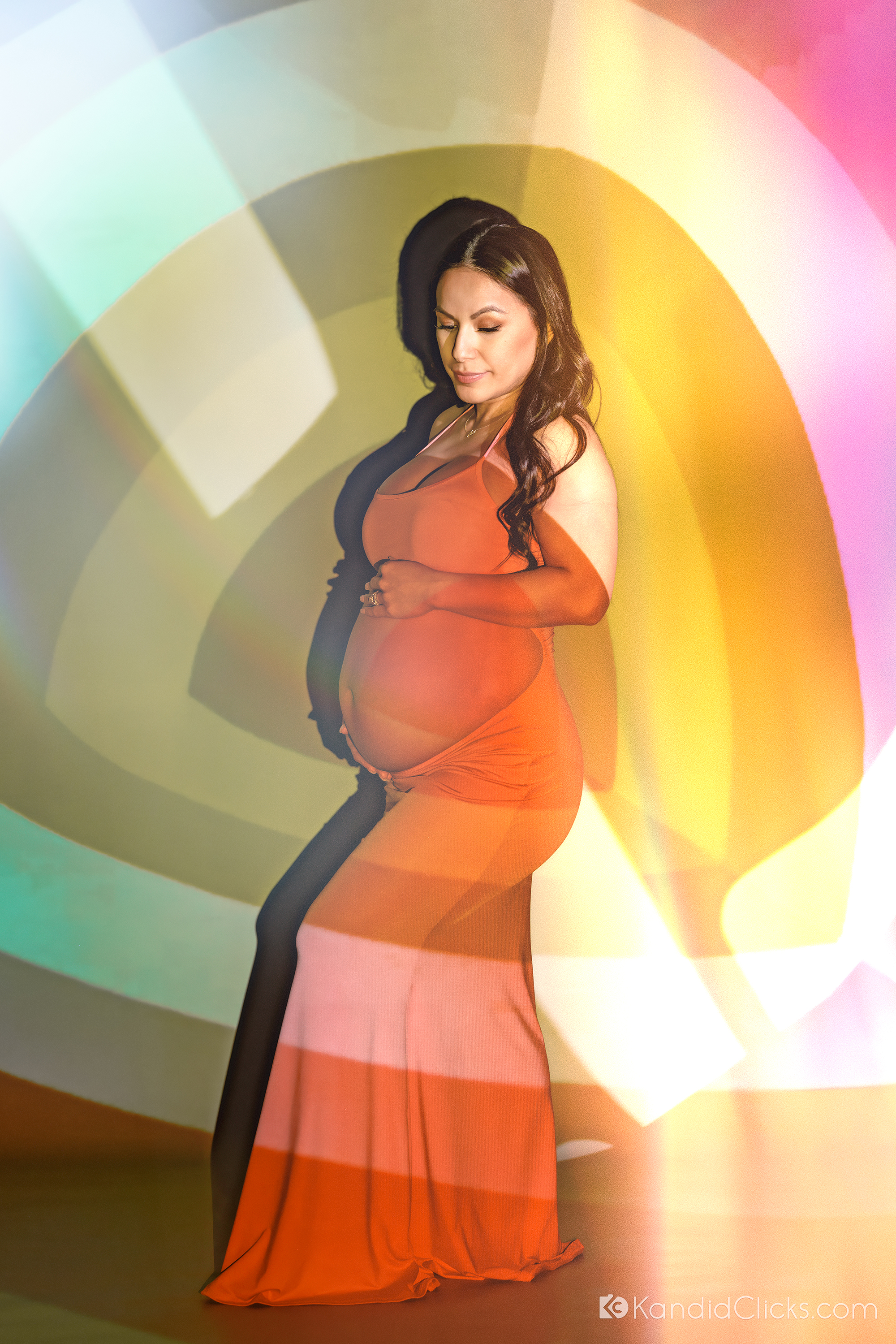 Maternity photographer captures expectant mother in red dress with vibrant studio light effects