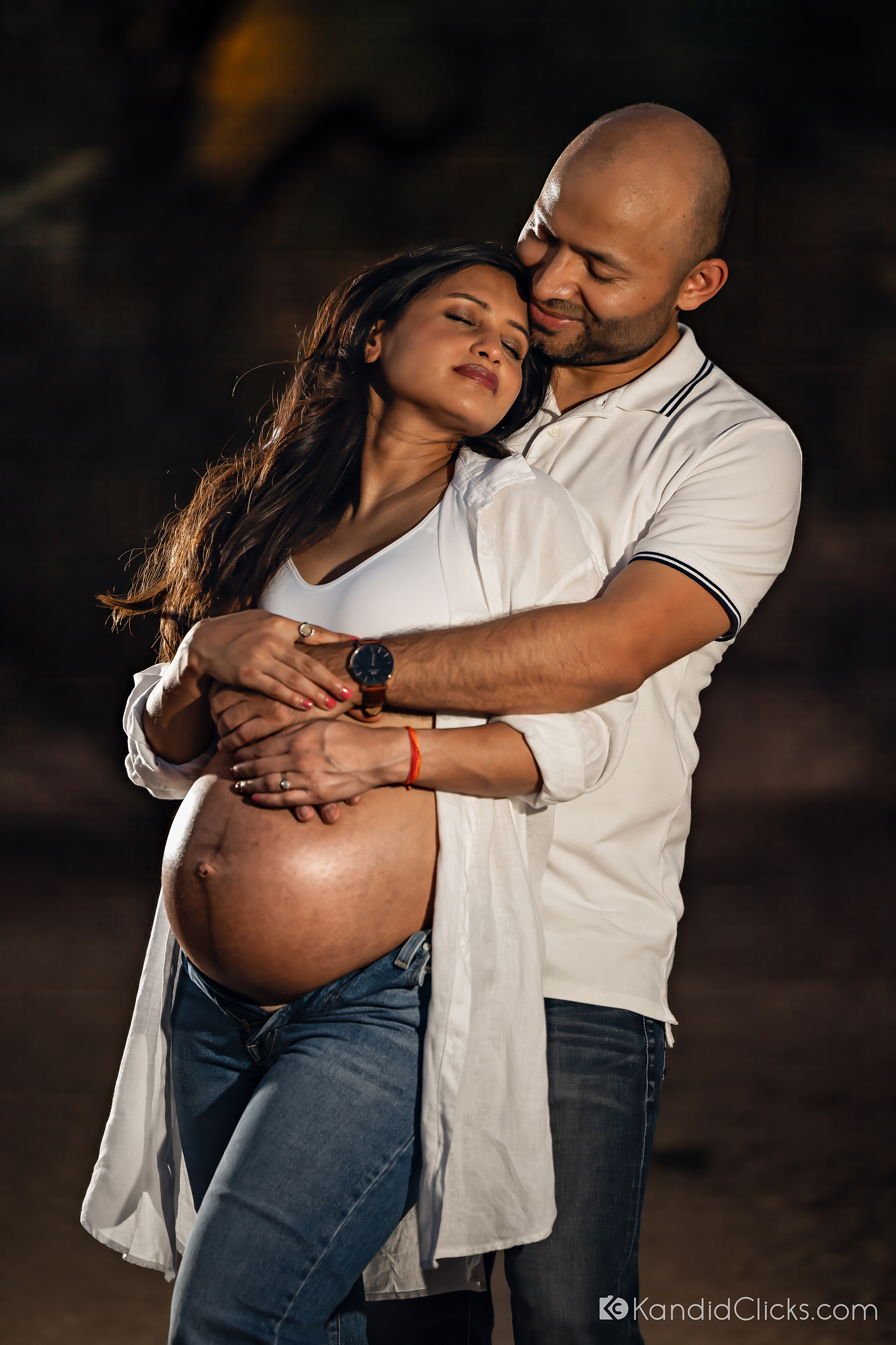 Maternity photographer captures quiet emotional moment of mom leaning into her partner’s arms, holding her belly