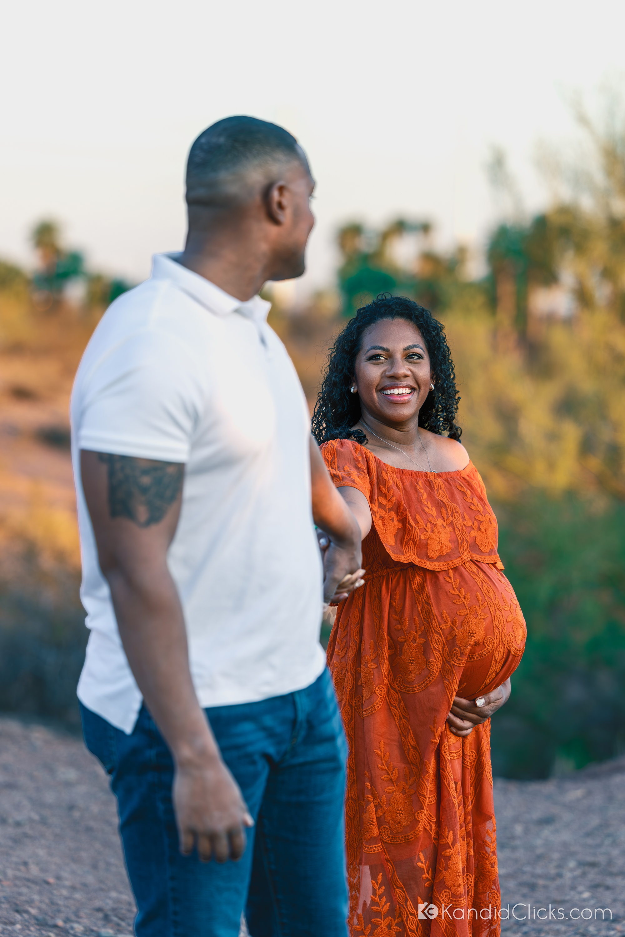 Maternity photographer captures expecting couple sharing a joyful moment, holding hands in nature