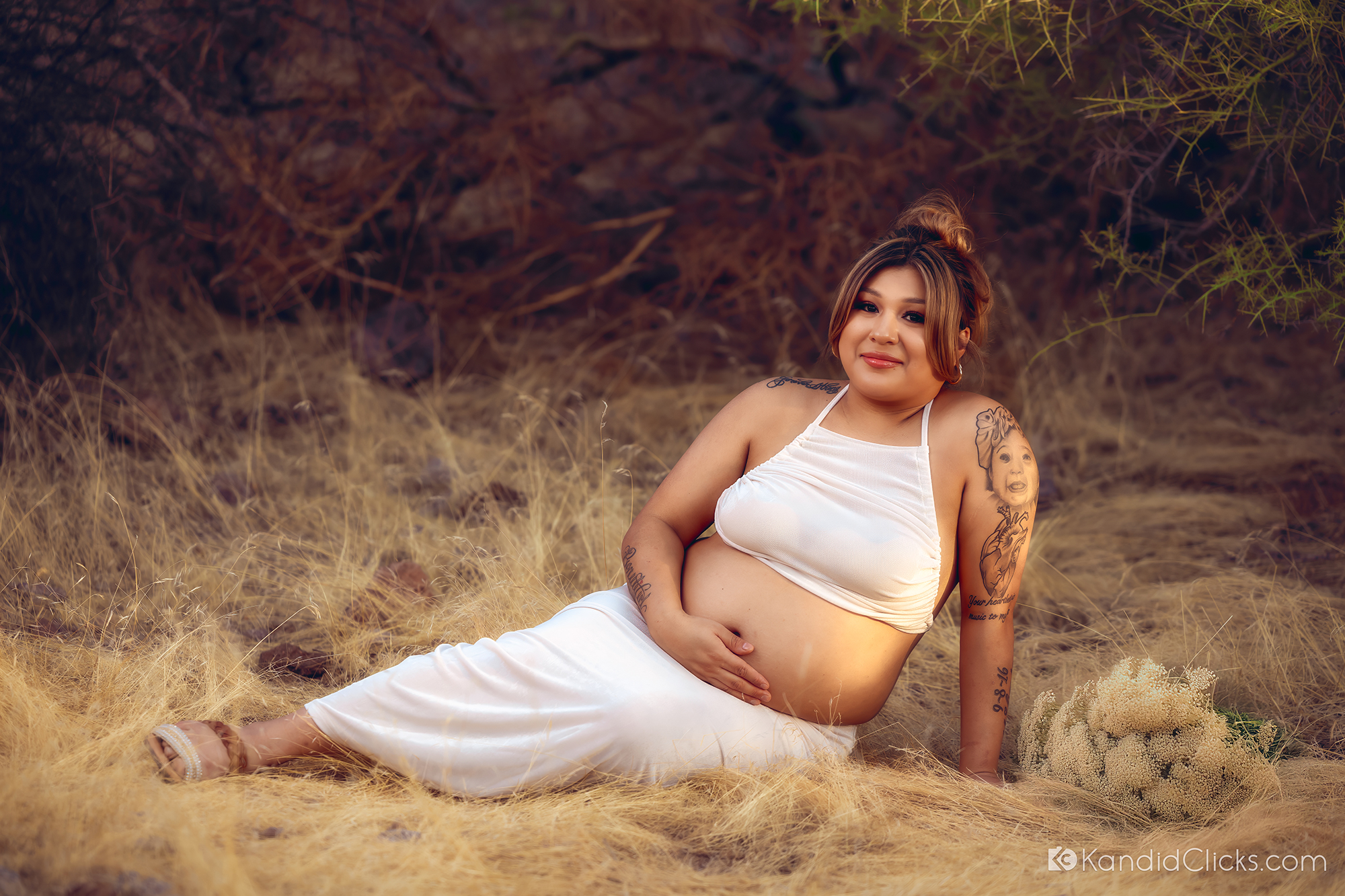 Maternity photographer captures mom-to-be in white dress reclining peacefully with bouquet in dry grass