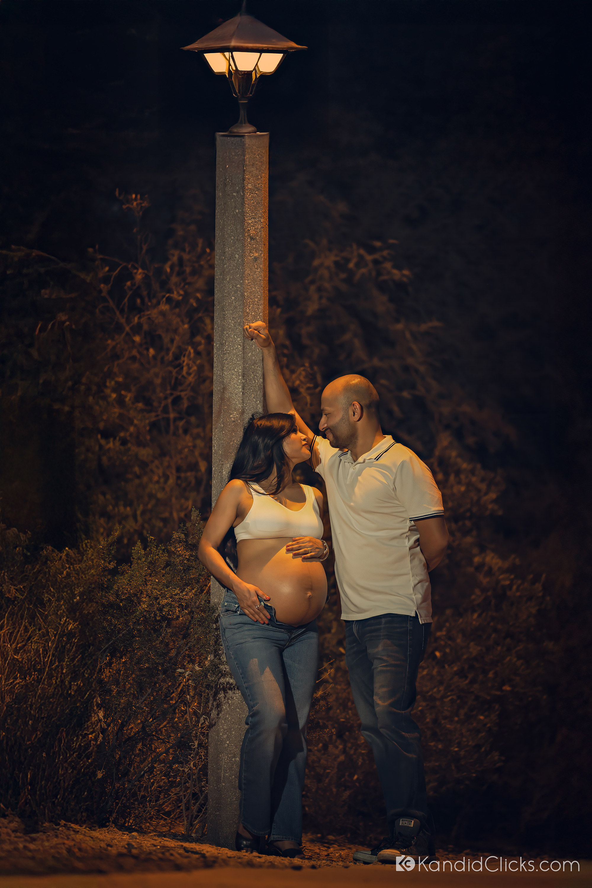 Maternity photographer captures a cozy evening moment of expecting couple standing beneath a lamp post