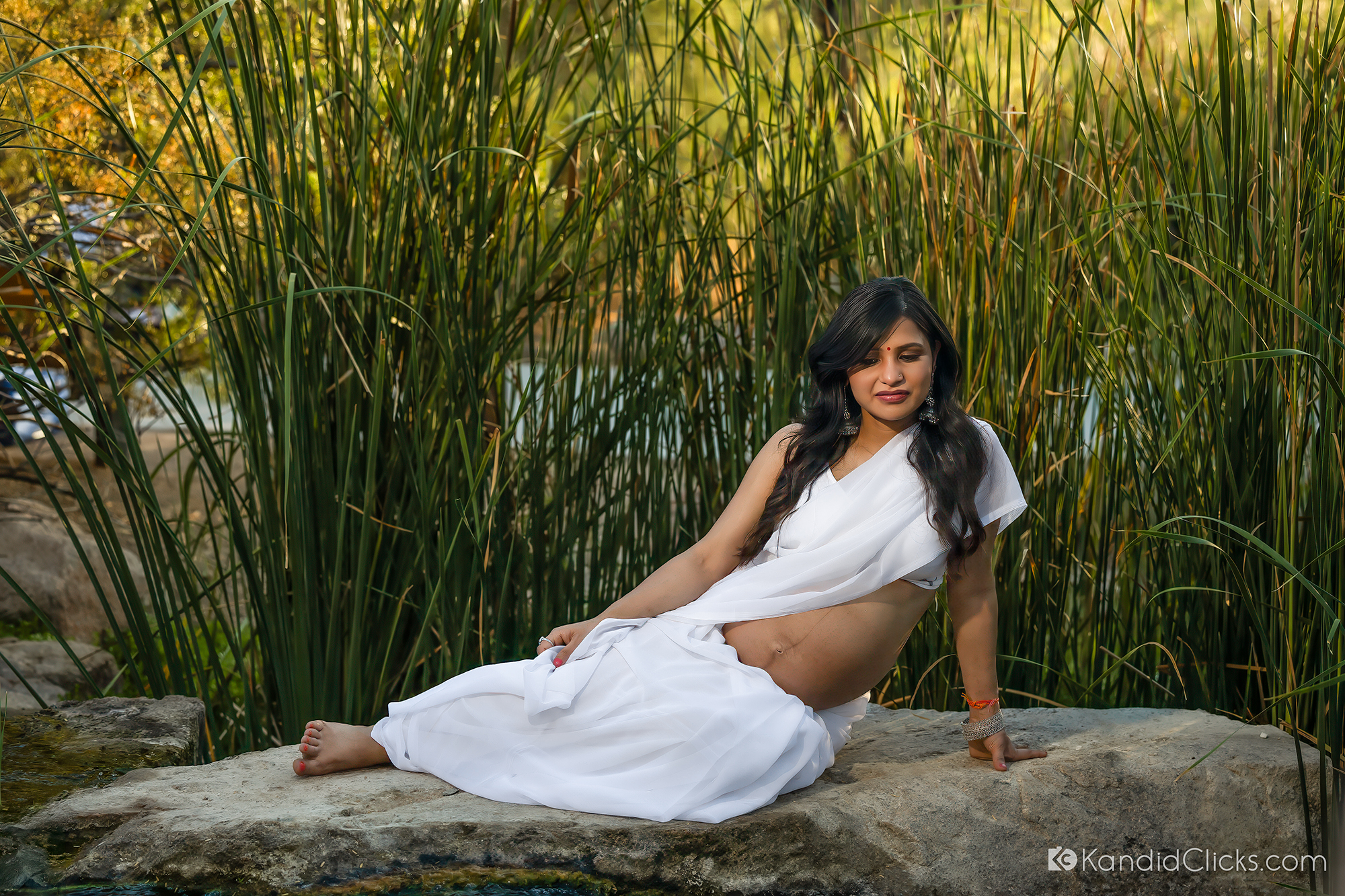 Maternity photographer captures a calm outdoor moment of a mother-to-be seated in white near tall grass