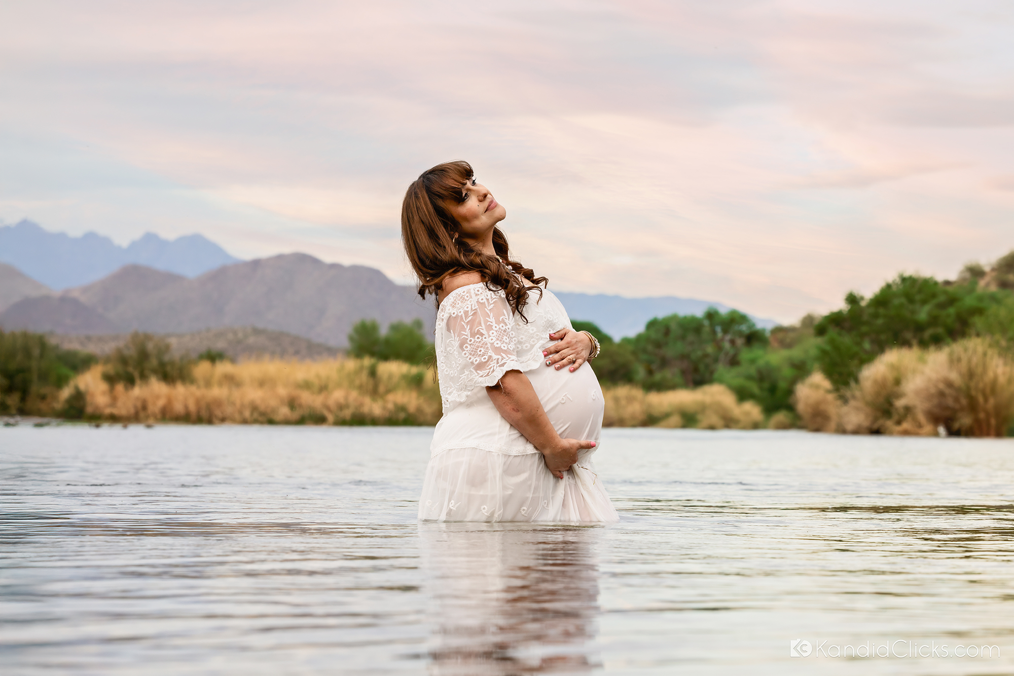 Maternity photographer captures mom-to-be in white dress standing in river during peaceful photo session