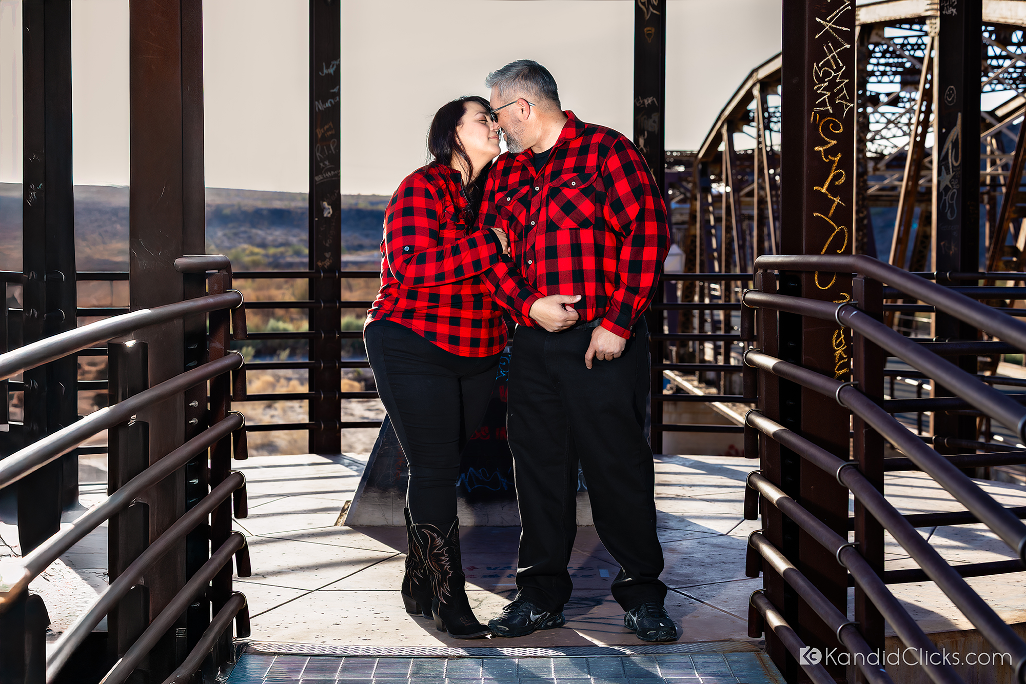 Couple in matching plaid shirts sharing a kiss during a casual engagement shoot in Arizona.