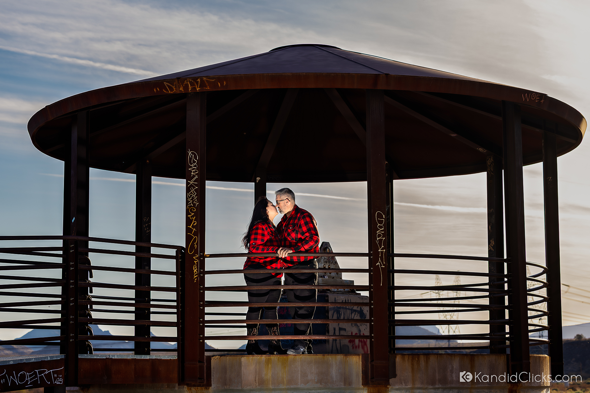 Couple kissing inside a gazebo while wearing matching red plaid shirts.
