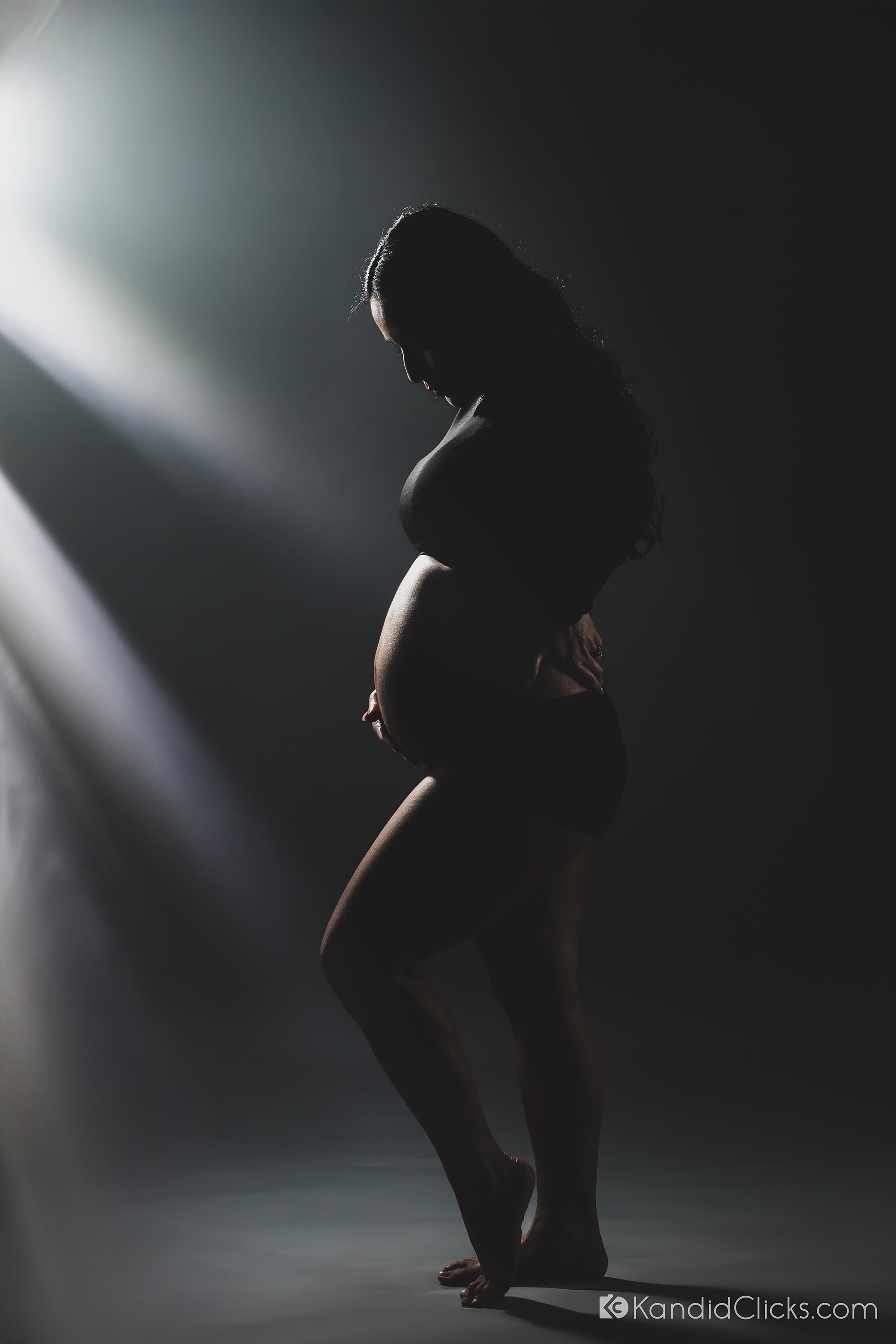 Studio maternity photographer captures expecting mother in moody silhouette under artistic lighting