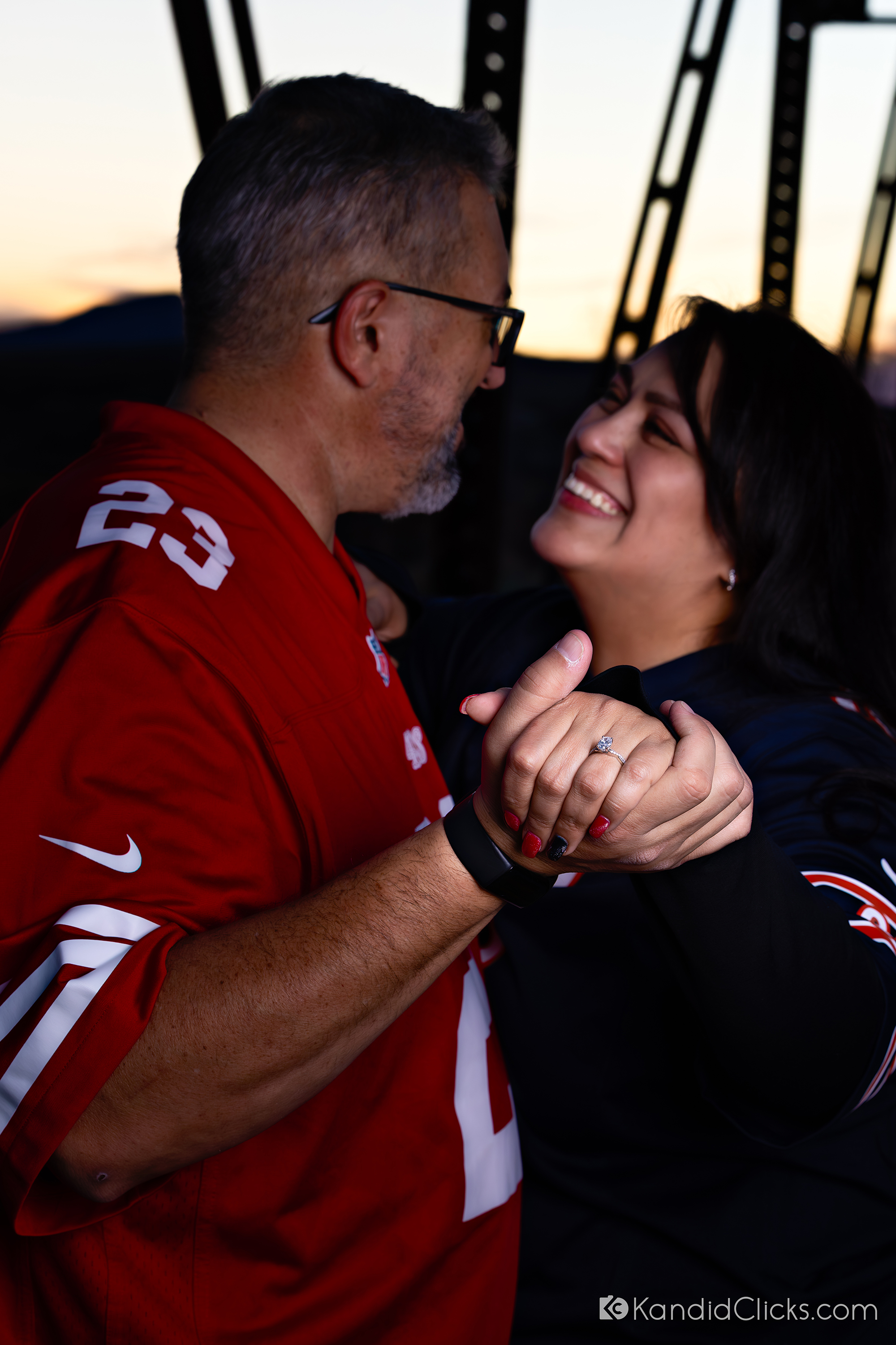 Smiling engaged couple holding hands during a sports-themed engagement shoot.