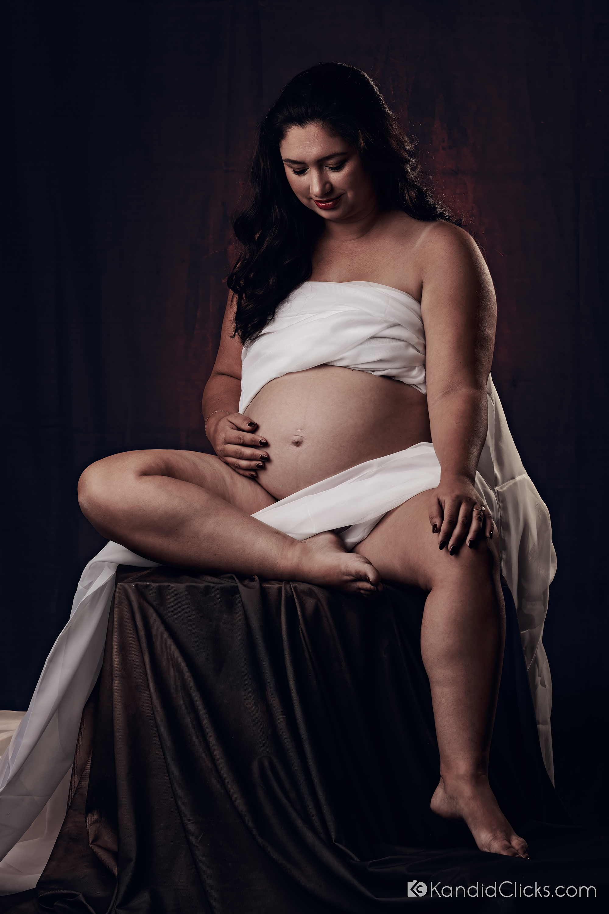 Pregnant woman in white fabric sitting gracefully in a studio maternity photo session