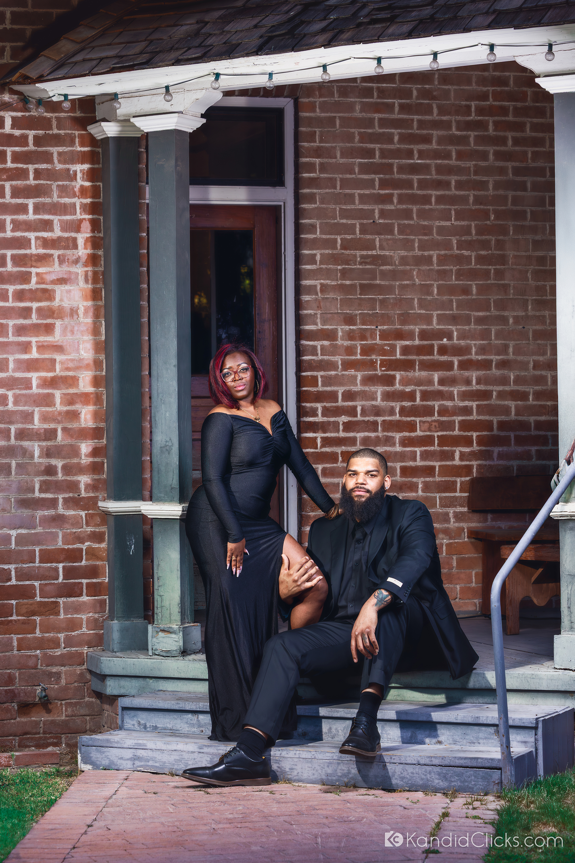Stylish Black couple posing on a rustic porch in formal black attire.