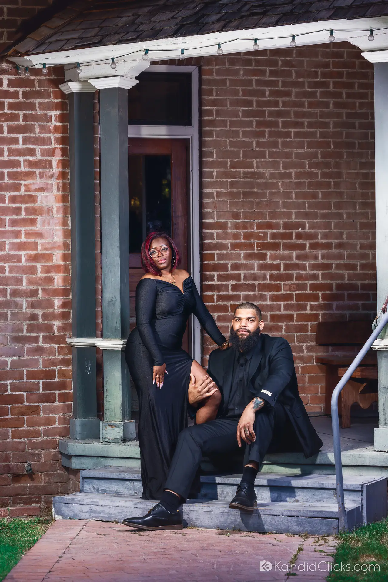 Stylish Black couple posing on a rustic porch in formal black attire.