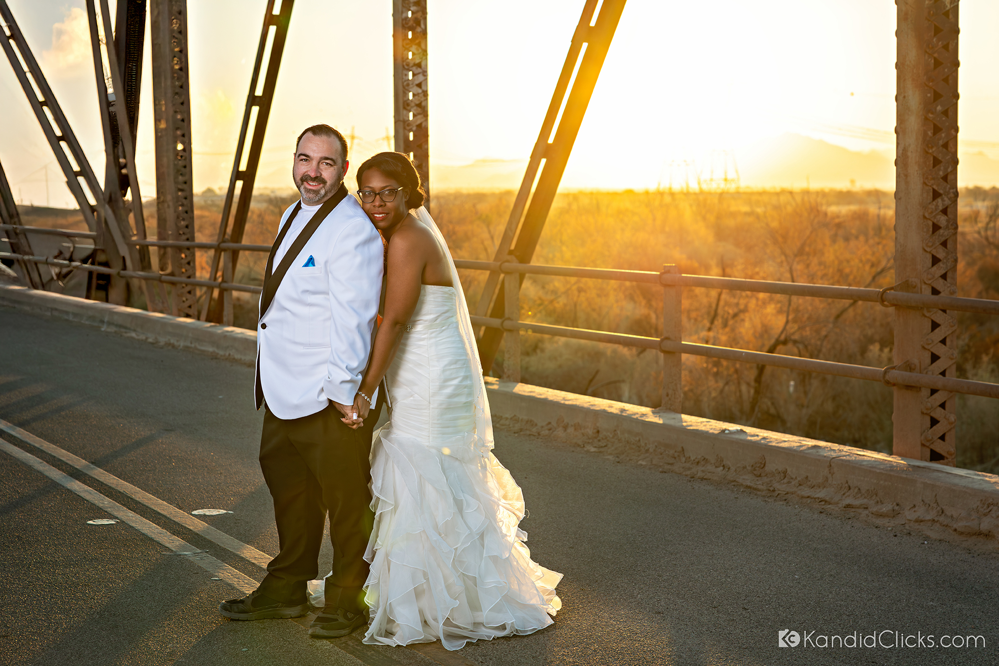 Bride and groom holding hands and smiling during a sunset wedding portrait on a bridge.