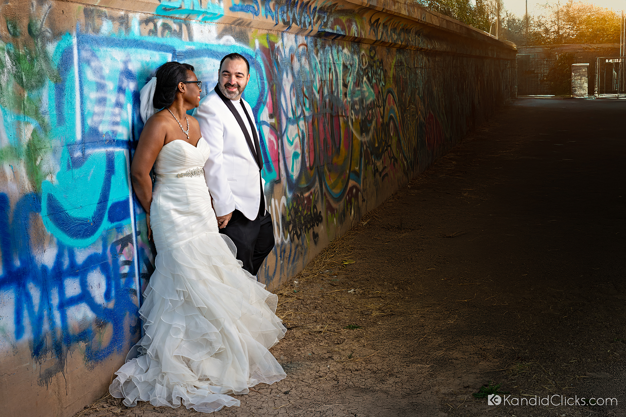Bride and groom leaning against a graffiti-covered wall in urban wedding shoot.