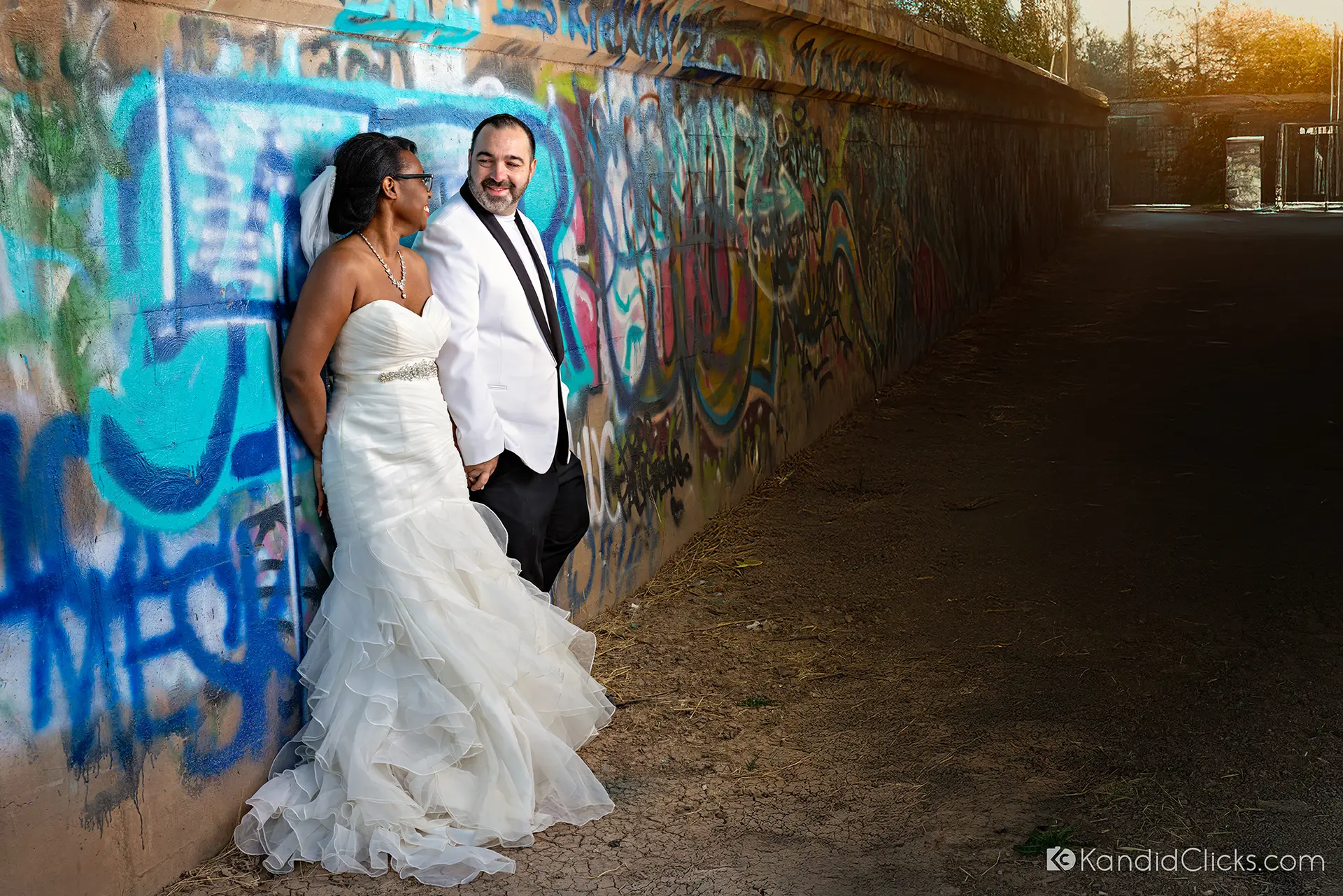 Bride and groom leaning against a graffiti-covered wall in urban wedding shoot.