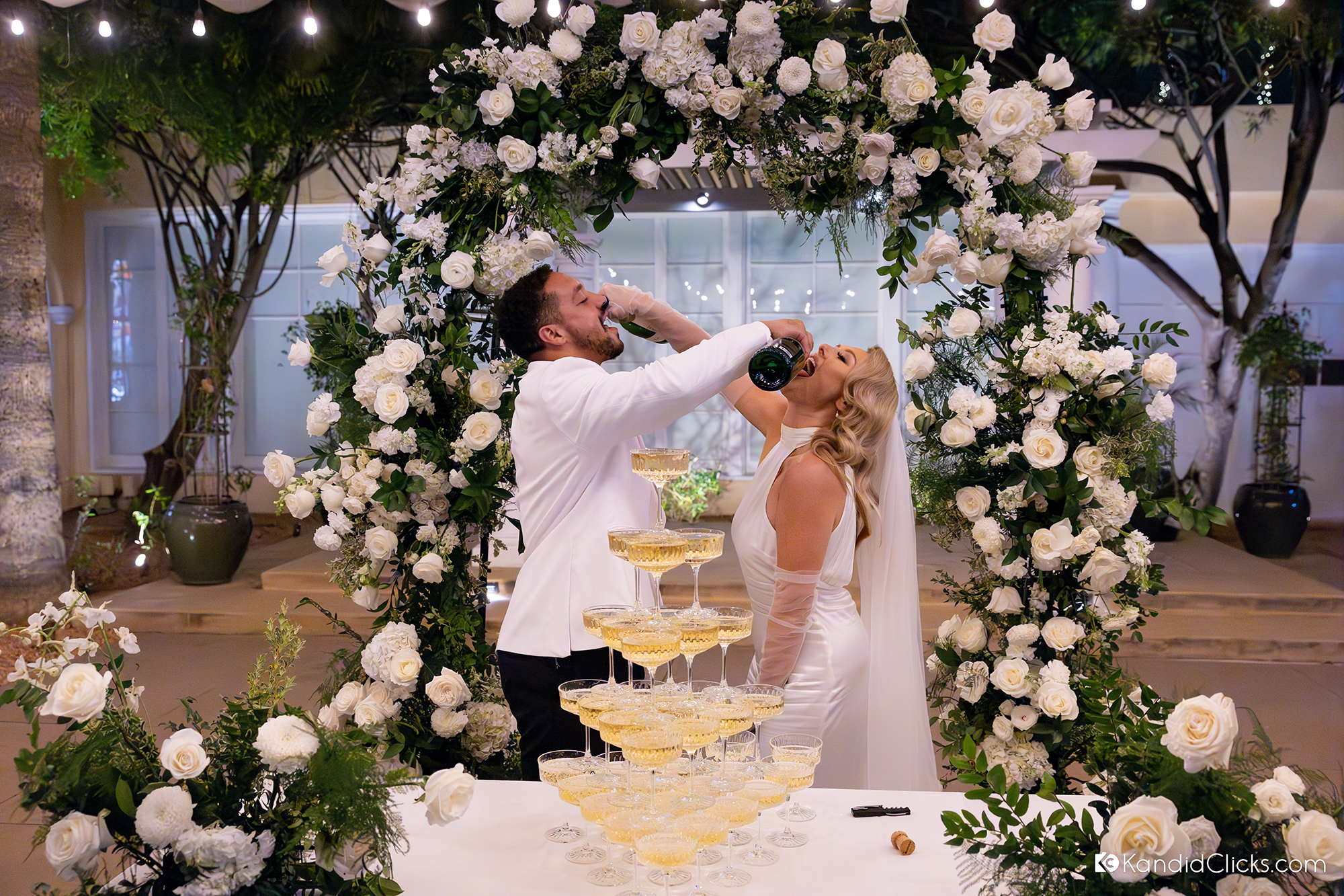 bride and groom drinking champagne fun wedding photo white floral arch