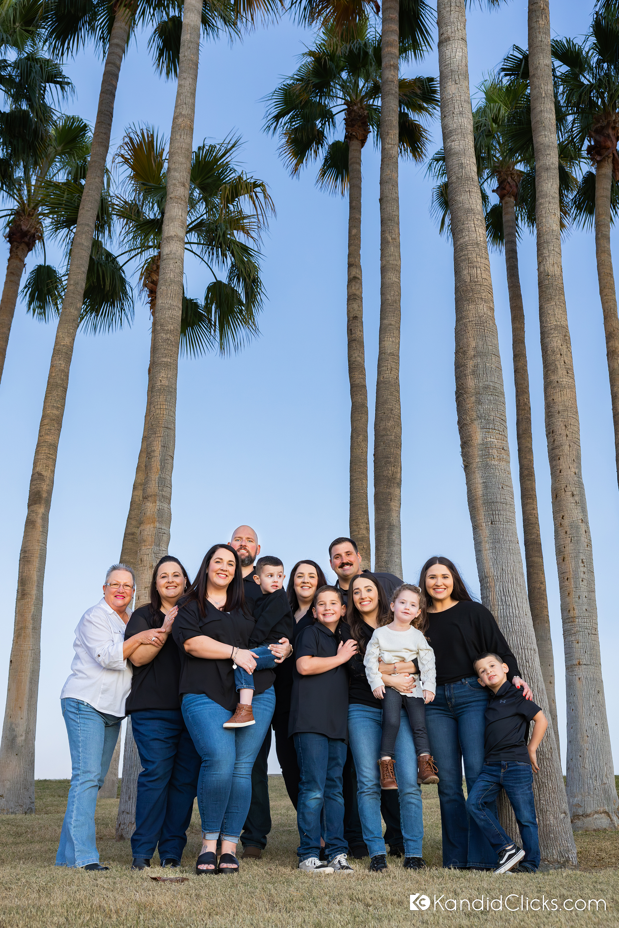 Smiling extended family standing close together during a kids photoshoot under palm trees in Arizona.