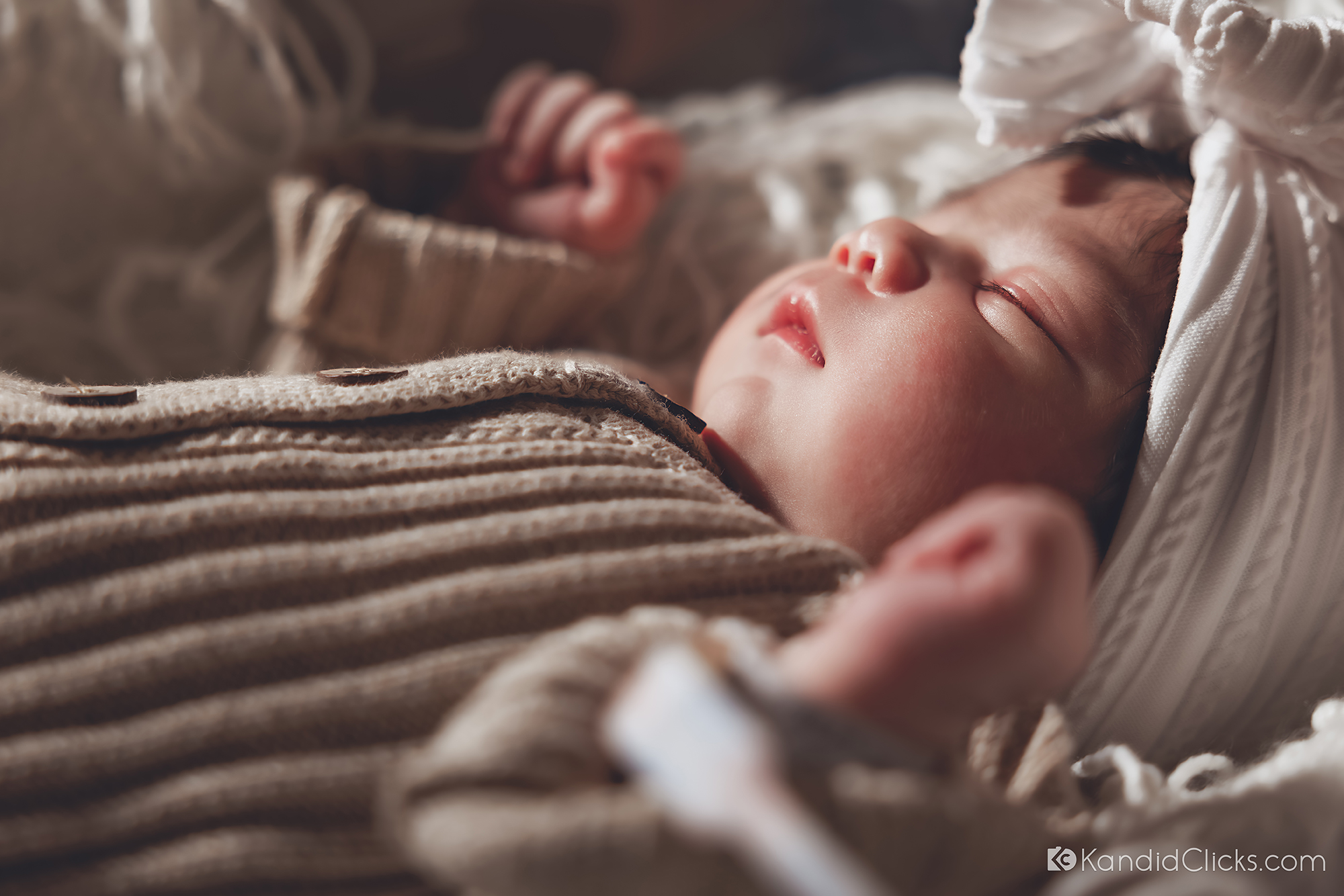 Close-up of sleeping newborn baby in natural light wearing a knit onesie and bow headband.