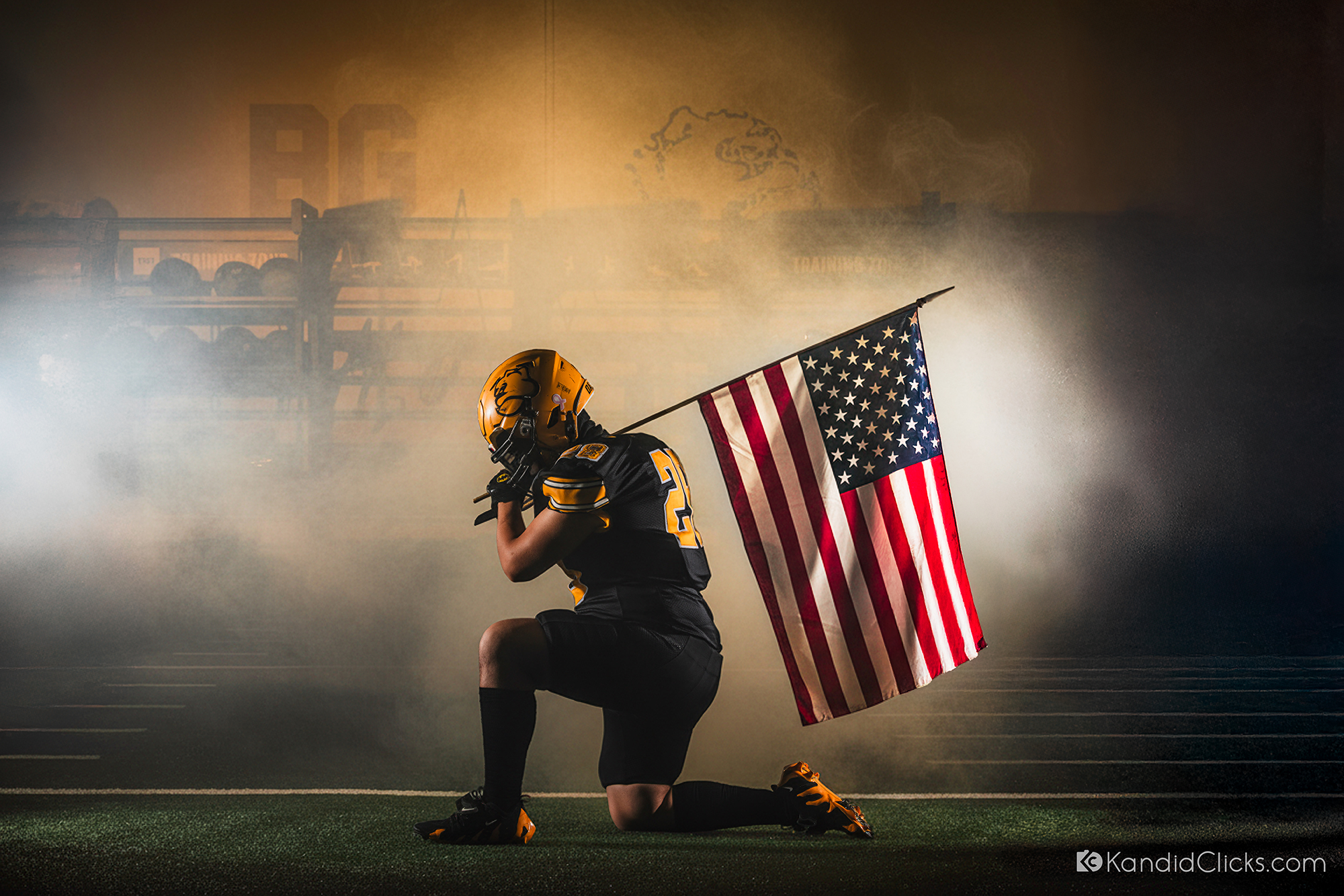 Football player kneeling on field holding American flag under dramatic stadium lighting