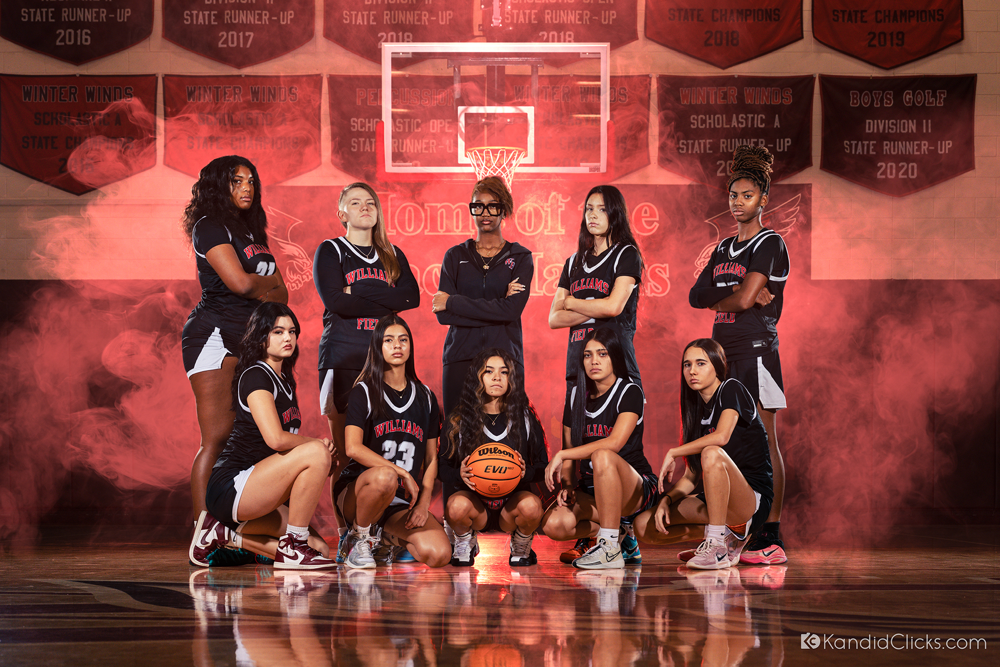 High school girls basketball team posing together in a gym with dramatic lighting and smoke effects