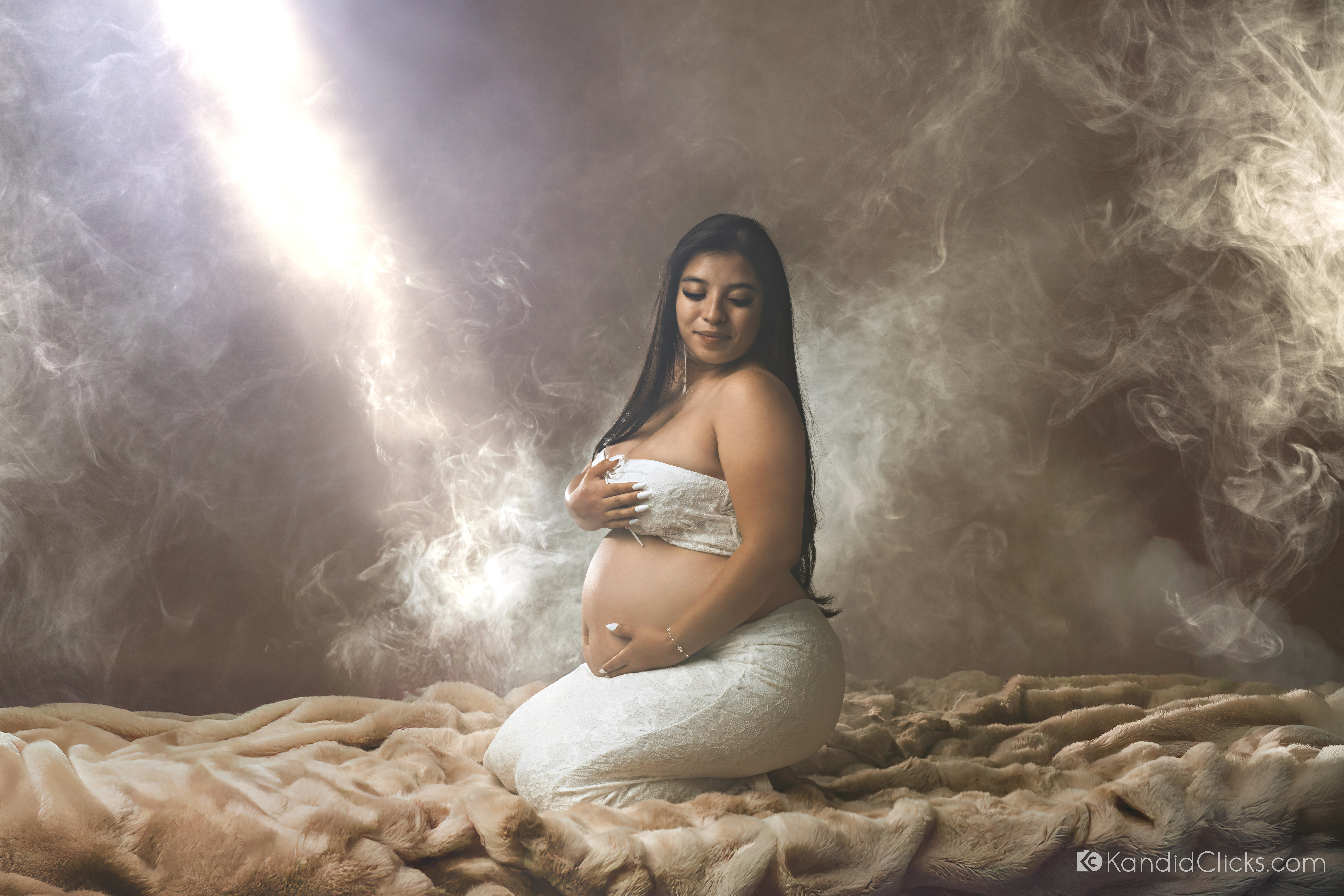 Dramatic fine-art maternity portrait of Shelby kneeling in a beam of light against an atmospheric backdrop.